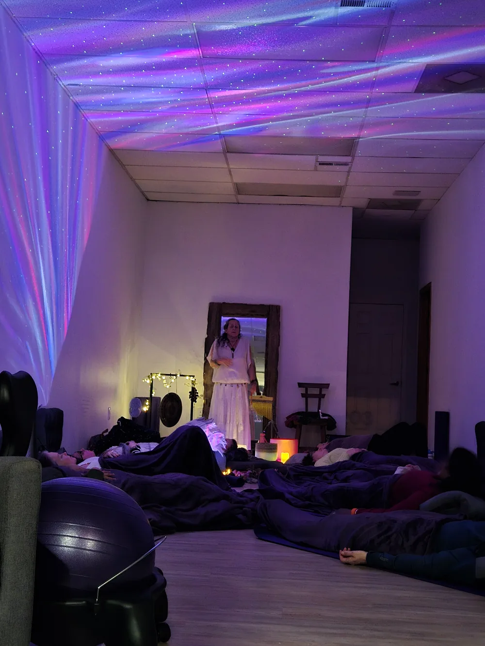 Amy guiding a sound bath in a starlit indoor room, with participants resting under blankets on the floor