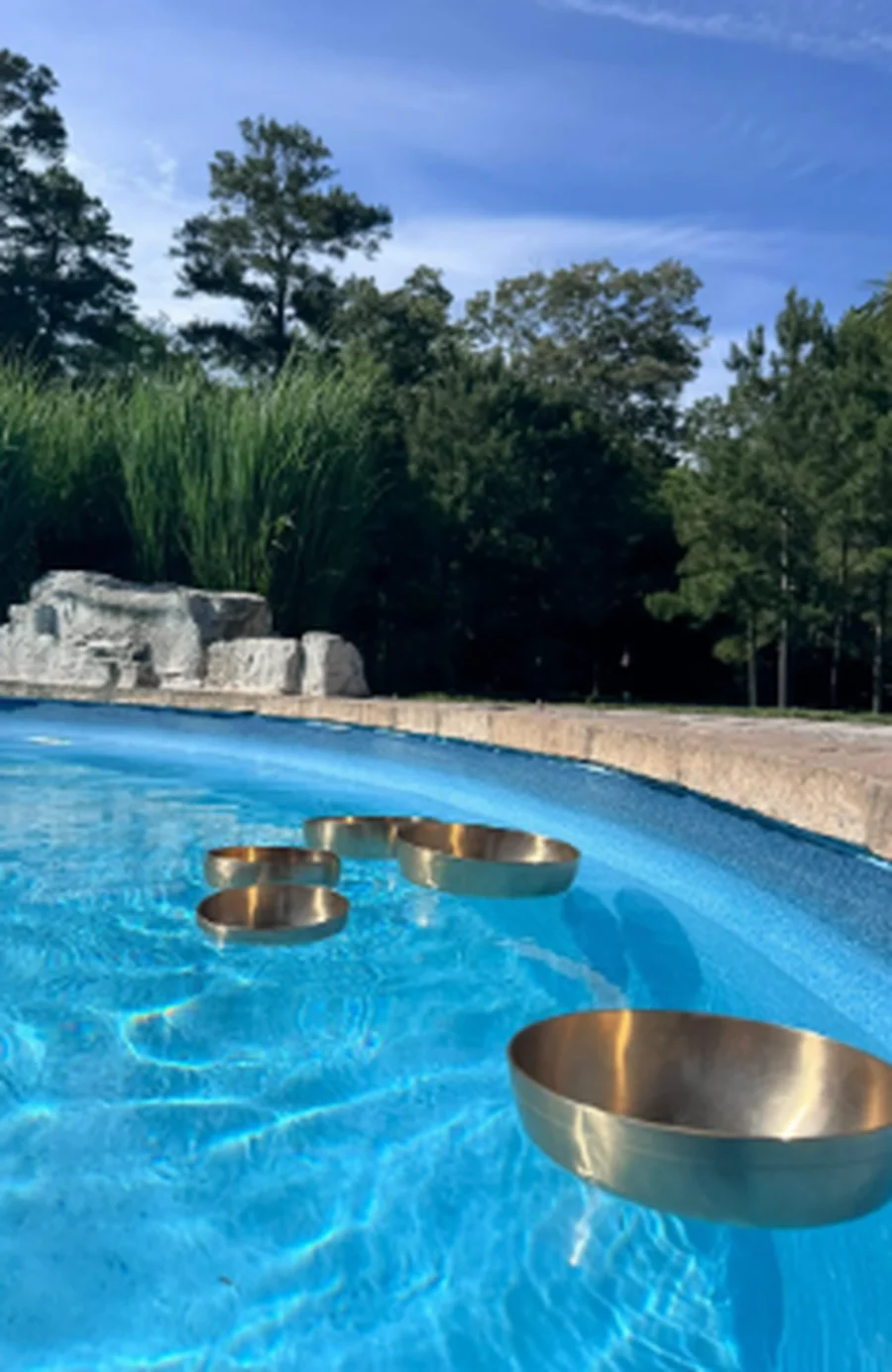 Crystal singing bowls floating on a sunlit pool, set up for a poolside sound bath